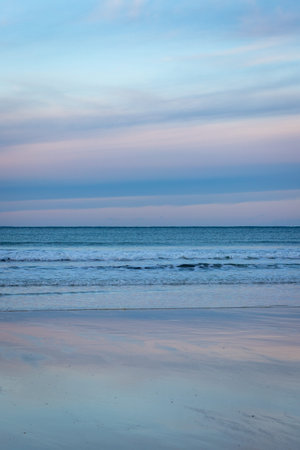 View to distant horizon over rolling waves with bright, vibrantly coloured sunset above reflected in...