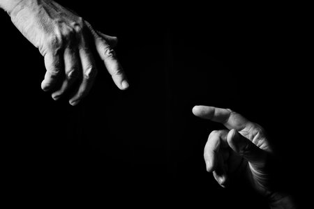 Black & white image of two male hands pointing or touching, as Creation of Adam, isolated against a black background with dramatic lighting.の写真素材
