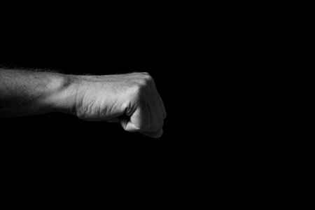 Black & white image of wrinkled male hand held out with clenched fist for fist bump or punch,...