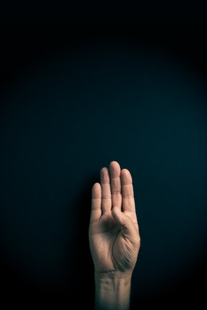 Dramatic colour image of male hand demonstrating ASL American sign language letter B with empty copy space for editorsの写真素材