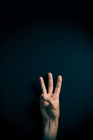 Dramatic colour image of male hand demonstrating ASL American sign language letter W with empty copy space for editorsの写真素材