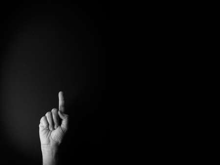 Dramatic black and white image of male hand demonstrating sign language number one against black background with empty copy space for editorsの写真素材