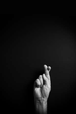 Dramatic B&W image of male hand demonstrating ASL American sign language letter R with empty copy space for editorsの写真素材