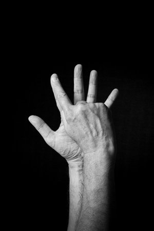 Dramatic B+W image of male hand fingerspelling BSL British sign language letter E isolated against dark backgroundの写真素材