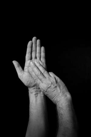 Dramatic B+W image of male hand fingerspelling BSL British sign language letter M isolated against dark backgroundの写真素材