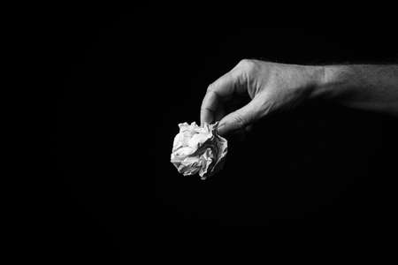 B+W image of male hand holding crumpled ball of paper against black background with dramatic lighting.の写真素材