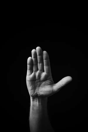 Dramatic B+W image of male hand fingerspelling CSL Chinese sign language letter U isolated against dark backgroundの写真素材