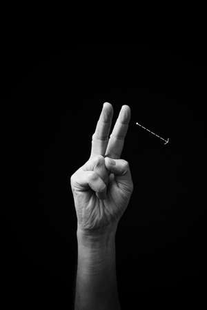 Dramatic black and white  image of a male hand fingerspelling the Ukrainian manual sign language letter 'Ð', isolated against a dark background.の写真素材