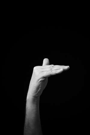 Dramatic black and white  image of a male hand fingerspelling the Ukrainian manual sign language letter 'Ð¤', isolated against a dark background.の写真素材