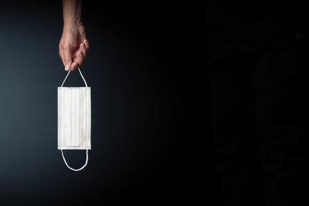 male hand holding single medical mask against dark background with copy space