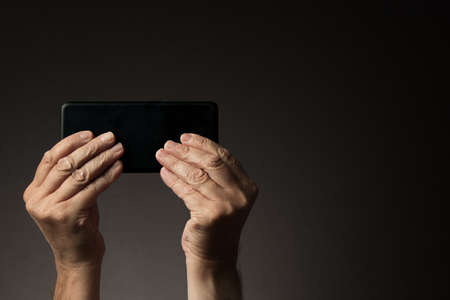Rear view of man's hands holding smart phone horizontally and texting or gaming isolated on dark background with copy spaceの写真素材