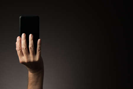 Rear view of man's hand holding smart phone isolated on dark background with copy spaceの写真素材