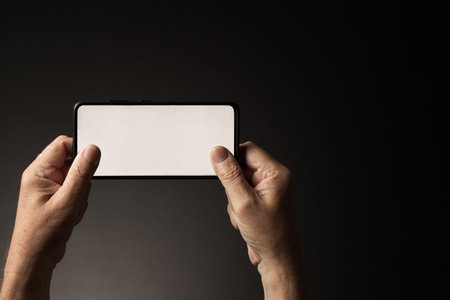 Man's hands holding smart phone horizontally texting or gaming with blank white screen isolated on...