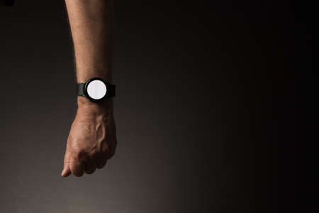 Man's hand with smart watch on wrist, displaying blank white screen, isolated on dark background with copy spaceの写真素材