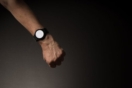 Man's hand with smart watch on wrist, displaying blank white screen, isolated on dark background...