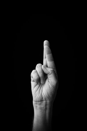 Dramatic black and white  image of a male hand fingerspelling the Japanese sign language letter 'RA' or 'ã', isolated against a dark background with copy space.の写真素材