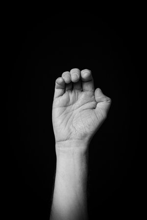 Dramatic black and white  image of a male hand fingerspelling the Arabic sign language letter 'Ø­'...