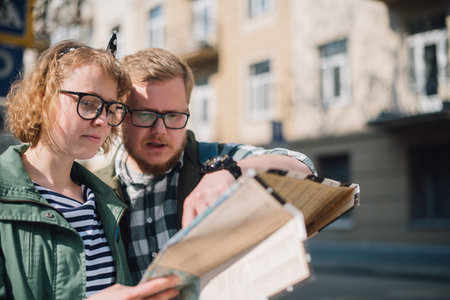 A young couple of tourists are looking for a road with a map in their hands in the city.