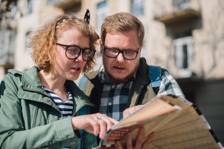 A young couple of tourists are looking for a road with a map in their hands in the city. of the city...