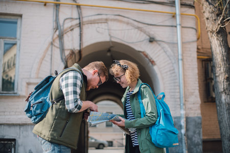 A young couple of tourists are looking for a road with a map in their hands in the city.