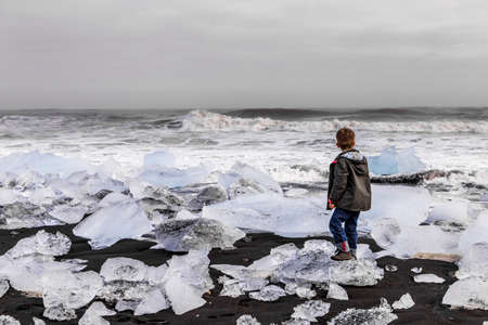 Young boy stay on black beach with ice in Icelandの写真素材