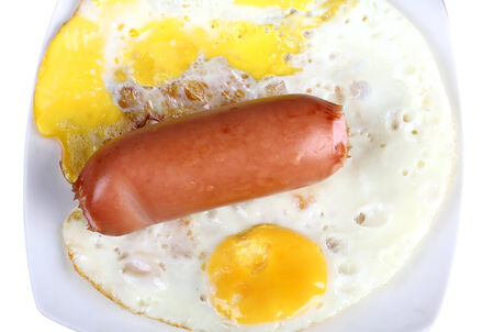 Fried eggs and sausage on a white porcelain plateの写真素材
