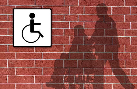Silhouettes wheelchair and man on a brick wallの写真素材
