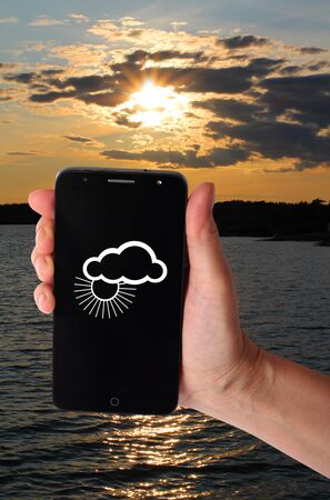 Smartphone in a female hand on a background of natural landscapes. Weather forecast imageの写真素材
