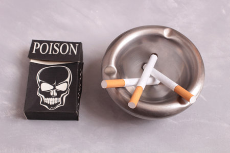 Metal ashtray and pack of cigarettes on stone background