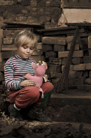 little girl with a toy in hands sitting on the ruins of a buildingの写真素材