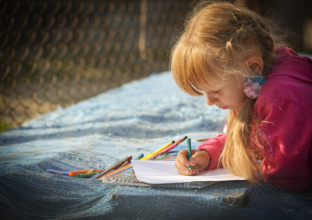 The girl in a red jacket draws a pencil on white paper  She leaned on the boards that are covered...