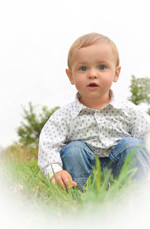 Little boy in a white shirt sitting in the green grassの写真素材
