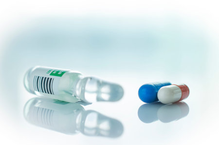 Glass vials of clear liquid and pills are on the light surface.