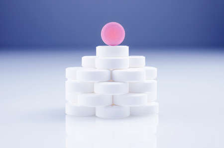 Heap of white tablets and one pink pill on the light surfaceの写真素材