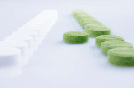 Close-up. Rows of white and green pills, standing opposite each other.  On the light surfaceの写真素材