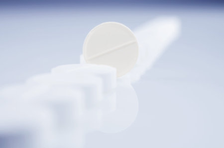 Close-up. One pill is standing upright in a series of white pills. On the bright surface