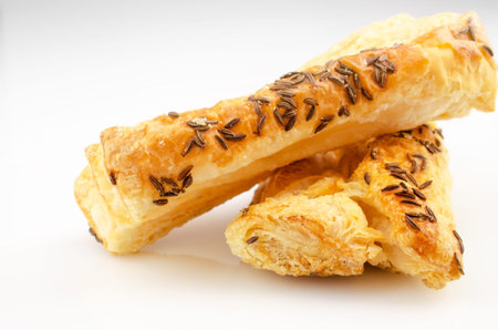 Confectionery theme. Puff pastry, topped with caraway seeds, on white surface.
