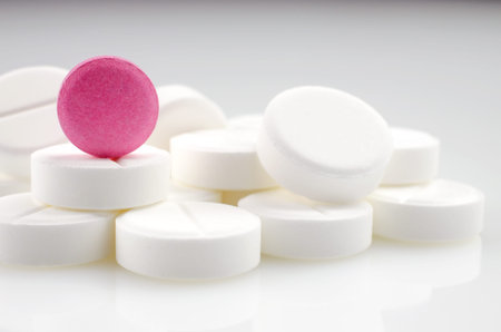 Close-up. Pink pill standing on a heap of white pills.