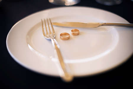 Two wedding rings lie on a white plate next to a knife and forkの写真素材