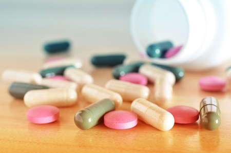 Pharmacy theme. White bottle of multicolored pills on a wooden surface. Closeup.の写真素材