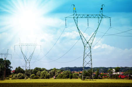 High voltage lines and power pylons in a flat and green agricultural landscape on a sunny day with cirrus clouds in the blue sky.の写真素材