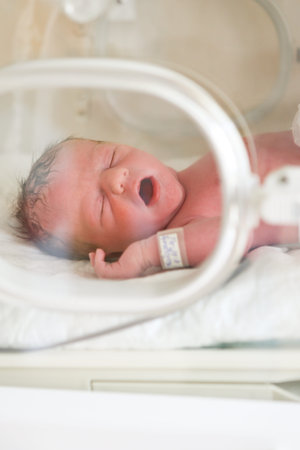 Newborn baby boy covered in vertix inside incubator