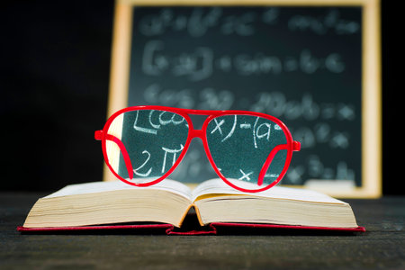 Red hipster glasses lying on a book on a chalkboard background with equations