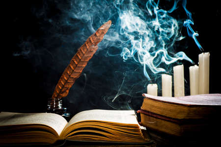 The concept of knowledge, an open book and an inkwell with a pen on the background of extinguished candlesの写真素材