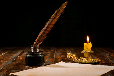 Education and writing concept, pen in ink bottle and candlestick with candle on wooden table on dark background.の写真素材