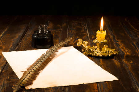 Education and writing concept, pen in ink bottle and candlestick with candle on wooden table on dark background.の写真素材