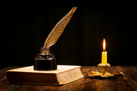 Education and writing concept, pen in ink bottle and candlestick with candle on wooden table on dark background.の写真素材