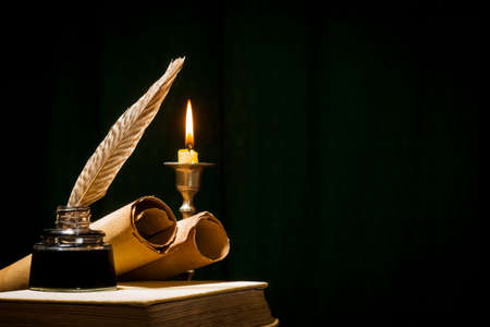 The concept of education and writing, a pen in an inkwell and a candle with a candle, and a book on a dark background.の写真素材