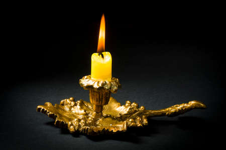 Vintage candlestick with a lit yellow candle on a black backgroundの写真素材