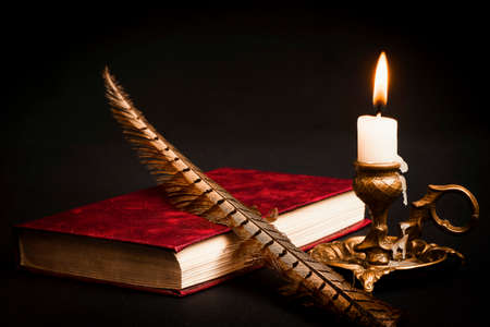 Pen on the book, and a lit candle in a candlestick on a black backgroundの写真素材